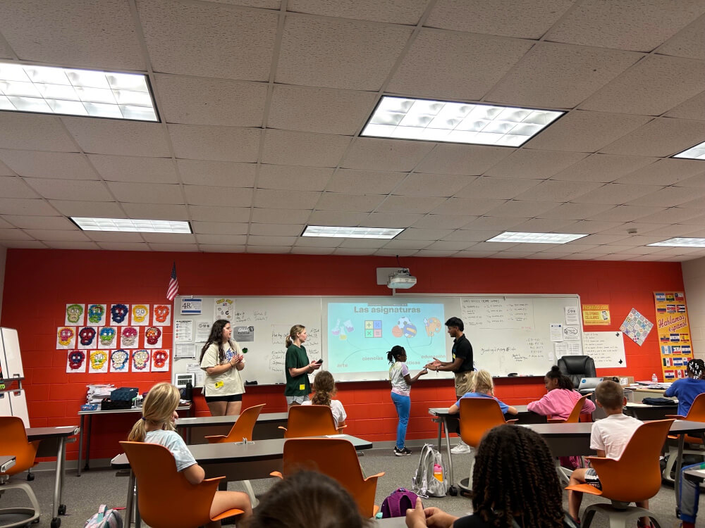 Group of people in a classroom. There is some text projected on the whiteboard.